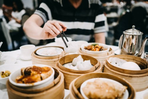 asian man picking up siu mai with chopsticks and enjoying a variety of freshly made dim sum in restaurant - junk food stockfoto's en -beelden