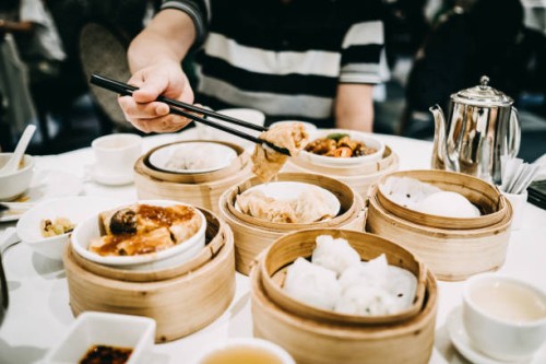 asian man picking up steamed beancurd roll with chopsticks and enjoying a variety of dim sum in restaurant - junk food stockfoto's en -beelden