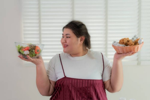 asian overweight woman holding salad in right hand and fries chicken in left hand, choosing healthy or unhealthy food nutrition . she looking happy to eat salad. concept of eating healthy or unhealthy lifestyle. - junk food s
