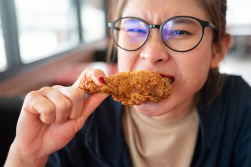 asian woman biting a pieces of fried chicken. - junk food stock pictures, royalty-free photos & images