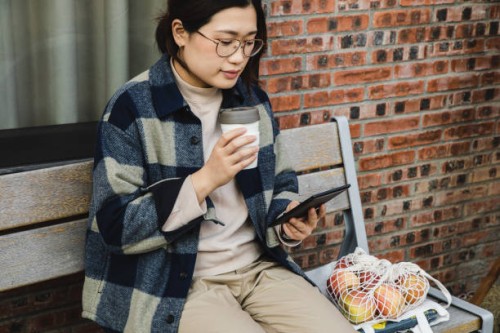 asian woman reading an e-book while drinking coffee using a reusable cup - junk food stock pictures, royalty-free photos & images