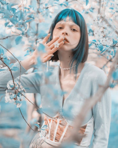 asian woman with blue hair on the background of a flowering tree. bang hairstyle. spring garden. white flowers - fashion stock pictures, royalty-free photos & images