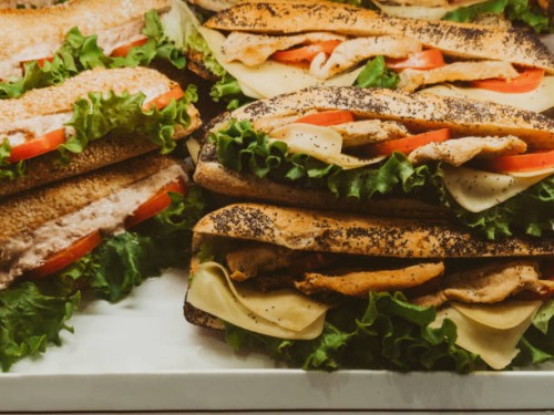 assortment of chicken sandwiches with cheese, tomatoes, and lettuce on display - junk food stock pictures, royalty-free photos & images