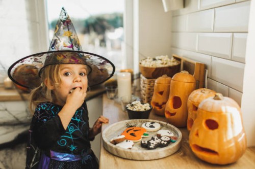 baby girl in witch costume stealing sweets from halloween table and eating. happy childhood - food stock pictures, royalty-free photos & images