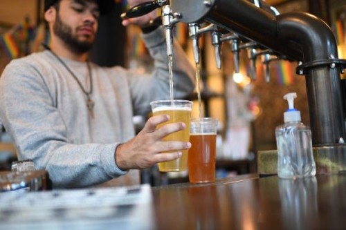Bartender pours pints for takeaway customers at The Ten Bells pub in east London on June 27, 2020. - The pub serves drinks for takeaway to maintain...