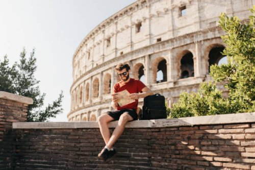 bearded male tourist reading map and smiling with colosseum in background - travel stock pictures, royalty-free photos & images