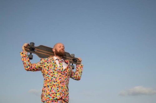 bearded man with longboard on his shoulders wearing suit with colourful polka-dots - fashion stock pictures, royalty-free photos & images