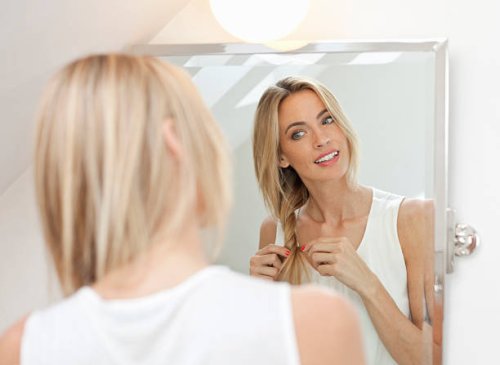 beautiful blonde doing her hair in front of mirror - hairstyle stock pictures, royalty-free photos & images