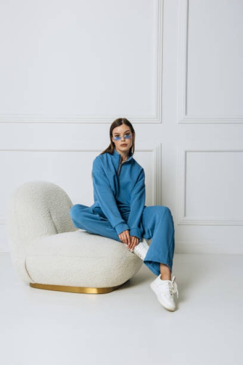 beautiful fashion model woman in glasses posing sitting in a chair in a room in a new collection of clothes. lady in room looking at camera in studio shot - fashion stock pictures, royalty-free photos & images