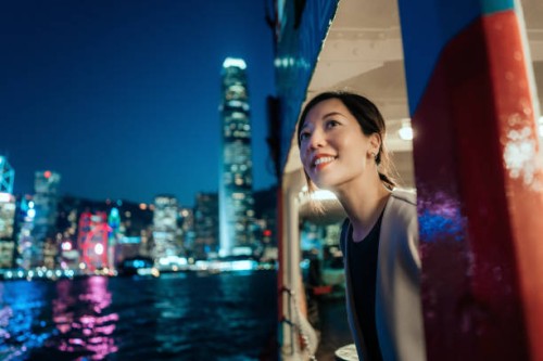 beautiful smiling young asian woman looking out through the window, enjoying spectacular illuminated night view of the city while travelling by ferry - travel stock-fotos und bilder
