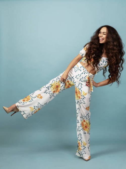 beautiful woman with long curly hair in floral outfit front of blue background - fashion stock pictures, royalty-free photos & images