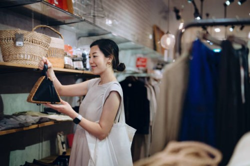 beautiful young asian woman shopping for personal accessories, looking at a handbag in boutique. sale season. seasonal shopping - fashion stock pictures, royalty-free photos & images