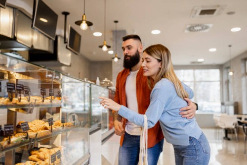 beautiful young couple is choosing pastries and smiling while doing shopping at the bakery - junk food stock pictures, royalty-free photos & images