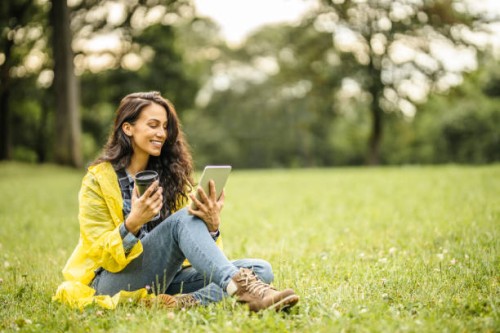 beautiful young lady in yellow raincoat reading a book on her digital tablet, drinking tea and sitting on grass while taking a break in nature - junk food stock pictures, royalty-free photos & images