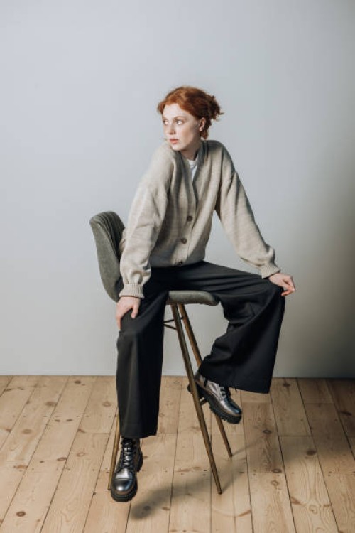 beautiful young redhead girl in a warm sweater and casual clothes sitting on a chair indoors - fashion stock pictures, royalty-free photos & images