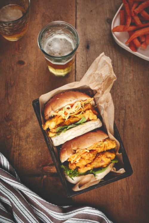 beer, burger and takeaway on a wooden table and fast food with chicken and diner meal. glass, alcohol and dinner with a basket or grill with luxury or eating with restaurant and delicious with supper - junk food stock picture