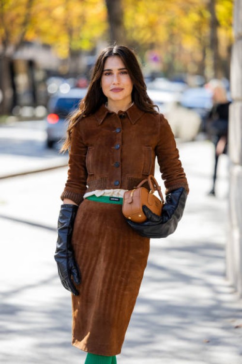 Belen Hostalet wears brown suede skirt, jacket, black gloves, bag, green knitted socks outside Miu Miu during Womenswear Spring/Summer 2025 as part...