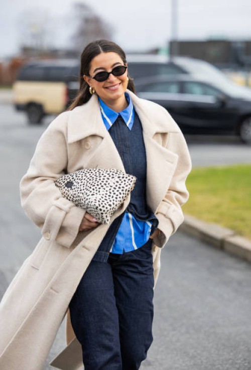 Benthe Liem wears beige coat, dark denim jeans, denim shirt, bag with dots print outside Marimekko during the Copenhagen Fashion Week Autumn/Winter...