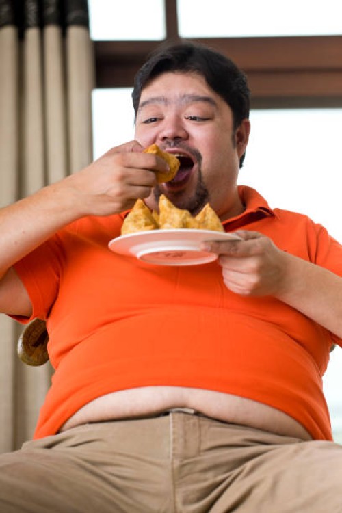 übergewichtiger mann isst samosa - junk food stock-fotos und bilder