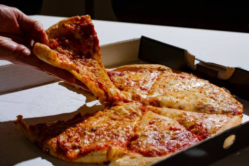 Berlin, Germany Symbolic photo on the subject of unhealthy food. A piece of pizza with a lot of cheese is taken out of a pizza box on February 13,...