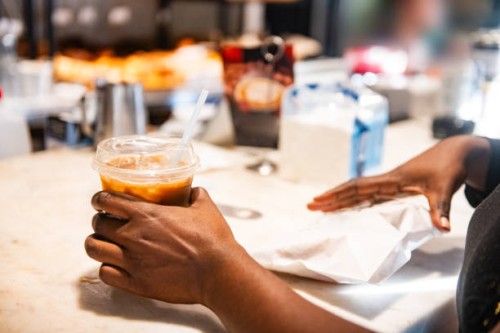 black woman's hands picking up iced coffee and snack from take out counter - junk food stock pictures, royalty-free photos & images