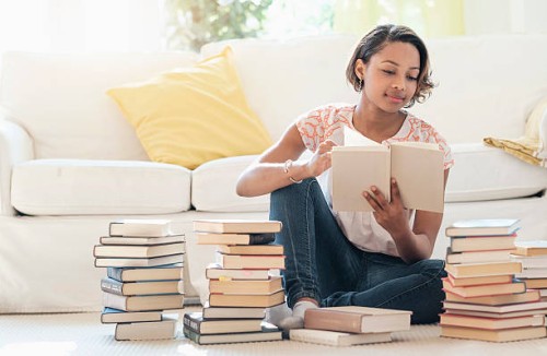 black woman sitting on floor reading pile of books - home decoration stock pictures, royalty-free photos & images