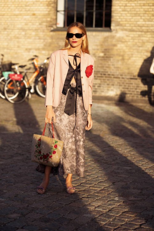 Blanca Miro Scrimieri wears a beige maxi skirt, black sheer blouse, pink blazer with a red flower, and black sunglasses outside Ganni during the...