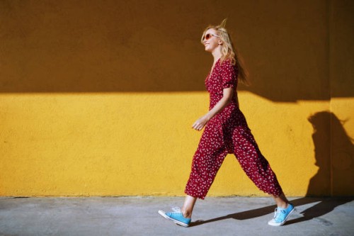 blond woman wearing burgundy jumpsuit and sunglasses while walking against the yellow wall - fashion photos et images de collection
