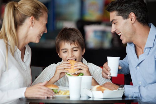 boy eating hamburger in fast food restaurant with his parents - junk food stock pictures, royalty-free photos & images