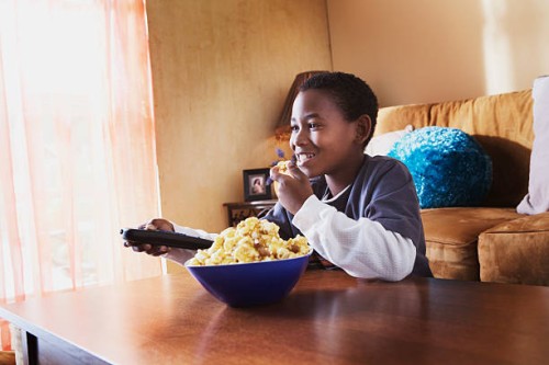 boy eating popcorn and watching tv - junk food stock pictures, royalty-free photos & images