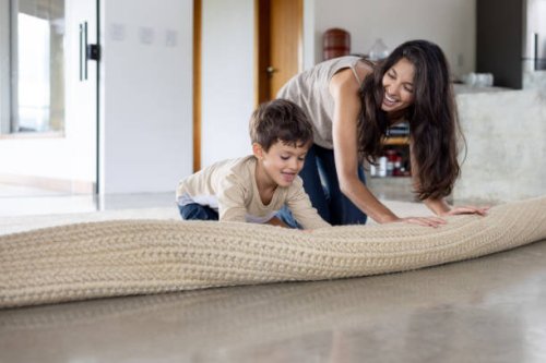 boy helping his mother unroll a carpet at home - home decoration stock pictures, royalty-free photos & images