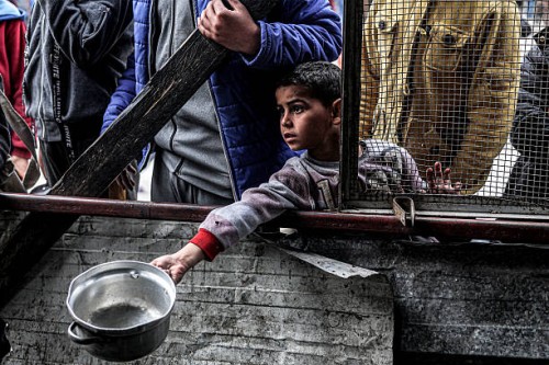 Boy holds out an empty pot as he waits with other displaced Palestinians queueing for meals provided by a charity organisation ahead of the...