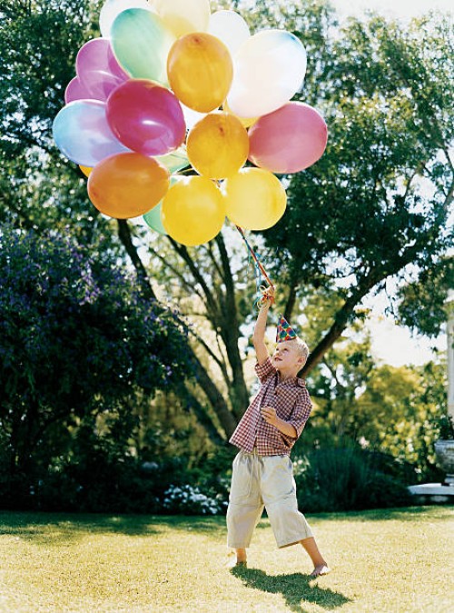 boy standing on the lawn holding a bunch of balloons - garden decoration stockfoto's en -beelden