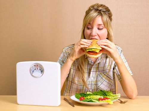 bulimic girl eating burger with bathroom scales - junk food stock pictures, royalty-free photos & images