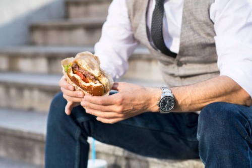 businessman in the city sitting on stairs eating a hamburger - junk food stockfoto's en -beelden
