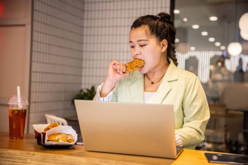 businesswoman eating fried chicken while working with laptop - junk food stock pictures, royalty-free photos & images