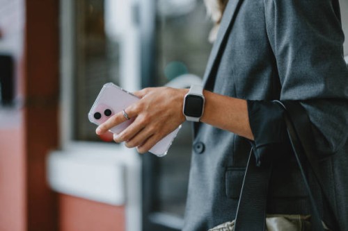 businesswoman holding smartwatch and smartphone in city street - fashion stock pictures, royalty-free photos & images