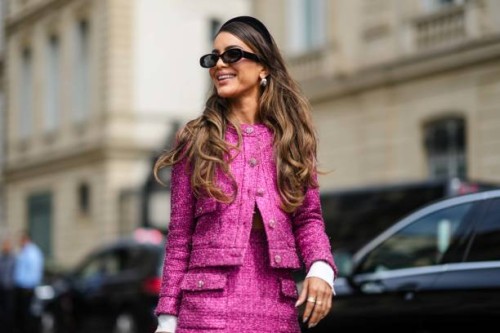 Camila Coelho wears a black velvet headband, black sunglasses, a pink tweed jacket from Chanel, a matching pink tweed short skirt from Chanel, a...
