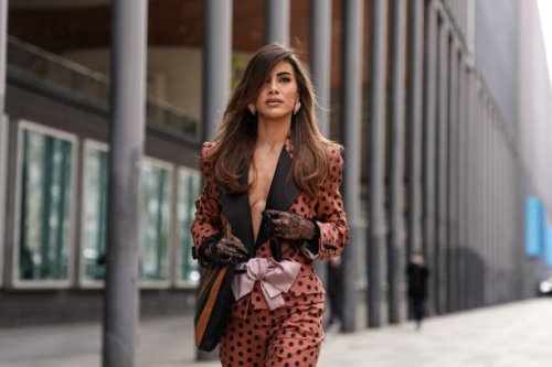 Camila Coelho wears light pink heart shaped earrings, dark brown black polka dotted light pink bow Valentino blazer jacket, black dark brown pattern...