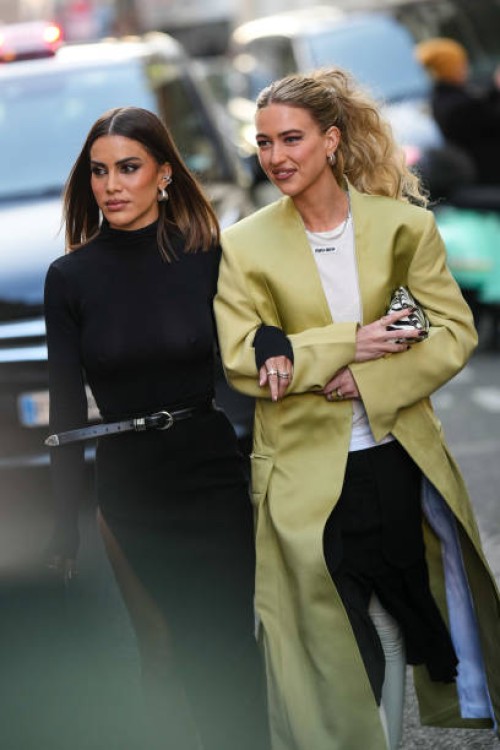 Camila Coelho wears silver large earrings, a black turtleneck / long sleeves tube long slit /split dress, a black shiny leather small belt, Emili...