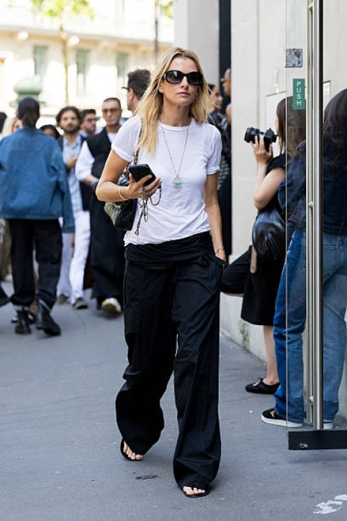 Camille Charriere wears a plain white crew neck t-shirt tucked into black low-rise wide-leg trousers, black thong sandals, a long pendant necklace,...