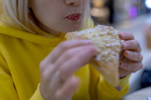 captured in exquisite detail, this photo showcases a woman's delightful bite into a cozy bun. the pastry's golden brown exterior contrasts beautifully with her softly glossed lips - junk food stock pictures, royalty-free phot