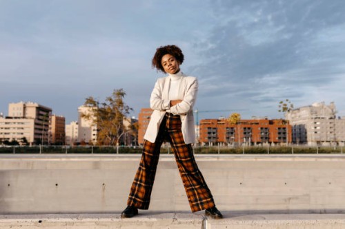 carefree afro woman with arms crossed posing on retaining wall against buildings in city - fashion stock pictures, royalty-free photos & images