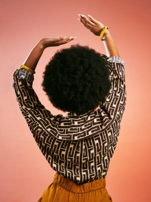 carefree fashionable retro woman dancing listening to music and having fun. portrait from behind of a funky and stylish female with afro hair isolated on a brown background. - fashion stock pictures, royalty-free photos & ima