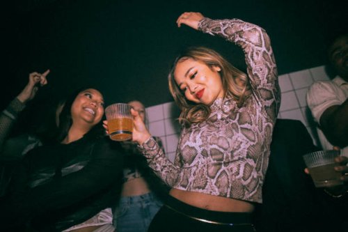 carefree young woman with drink dancing by female friend enjoying at nightclub - concert stock pictures, royalty-free photos & images