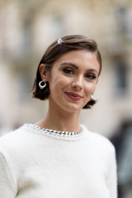 Carmella Rose wears silver hoop earrings and a white dress with a chain on the neck line outside Stella McCartney show during Womenswear...