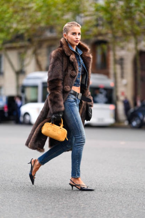 Caroline Daur wears silver earrings, black bandeau top, navy blue denim jean cropped jacket, black belt, washed navy blue denim jean skinny pants,...