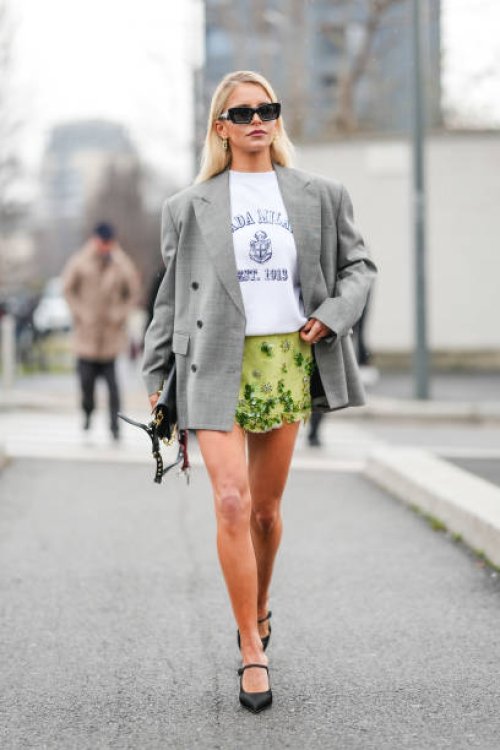 Caroline Daur wears silver earrings, white Prada purple t-shirt, light green floral beaded detail Prada mini skirt, black leather bag, light gray...