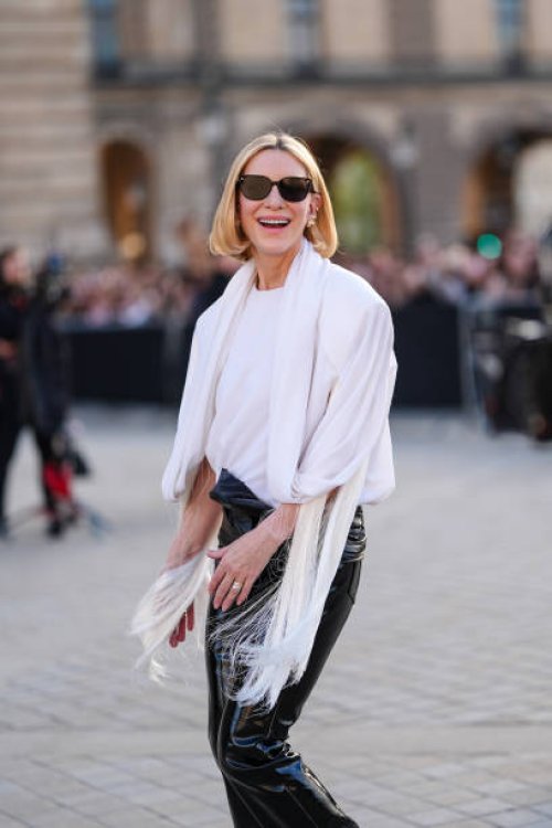 Cate Blanchett wears black sunglasses, white board shoulder draped Louis Vuitton top, shiny black wrapped Louis Vuitton leather pants, outside Louis...