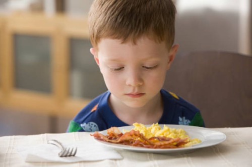 caucasian boy looking at plate of eggs and bacon - food stockfoto's en -beelden
